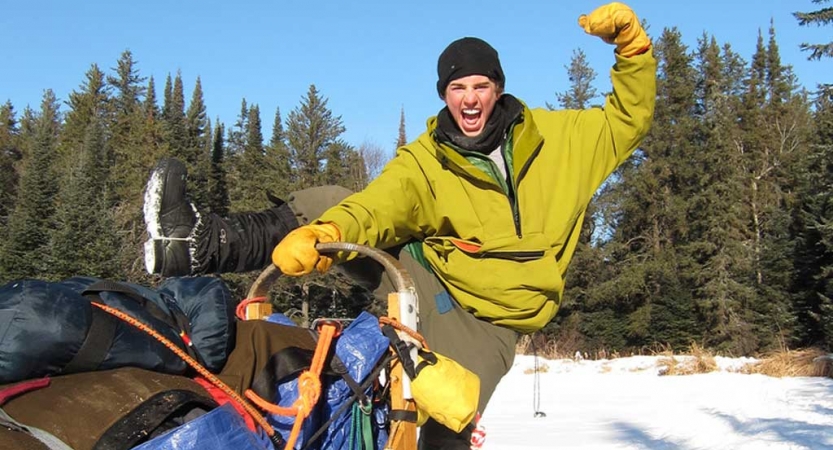 A person flexes their muscles while standing at the back of a dog sled
